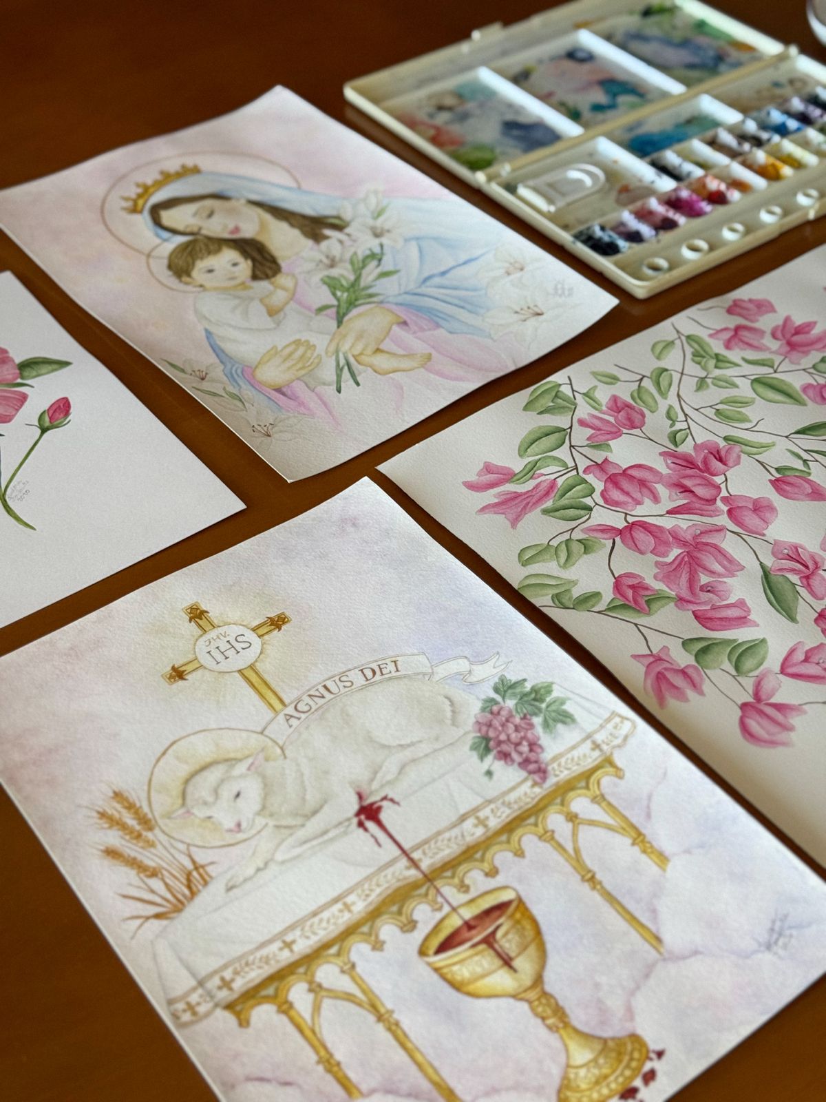 Aquarelas devocionais e florais dispostas sobre a mesa do ateliê